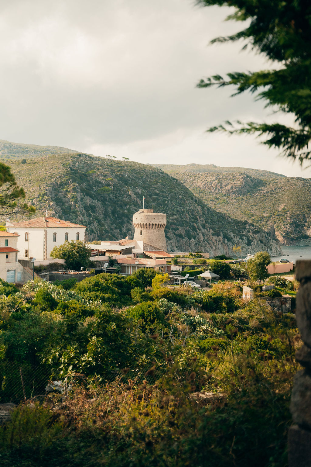 Una torre di pietra tra la macchia, con il mare dietro
